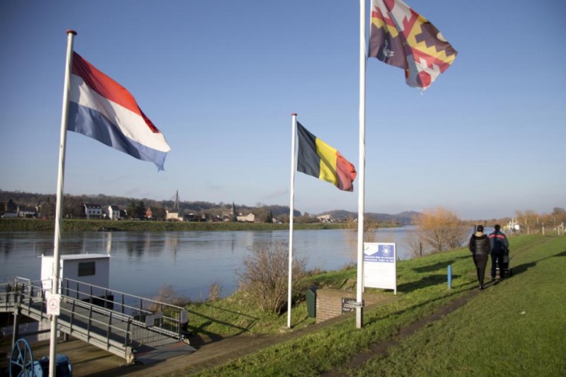 In this photo taken on Monday, Dec. 14, 2015, people walk past Dutch and Belgian flags on the waterfront in Eijsden, Netherlands. The town of Eijsden, in the Netherlands, has a short ferry which crosses the water to Lanaye, Belgium in a matter of minutes. While Belgium will be losing a splendid piece of nature that juts into the Meuse River dividing the two nations, it will also unburden itself of a jurisdictional nightmare that developed over time as the river meandered to turn the portion of land belonging to Belgium - about 15 soccer fields worth - into a peninsula linked only to the Netherlands. (AP Photo/Virginia Mayo)